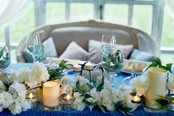 Table de mariage décorée de fleurs blanches, bougies. Canapé doux avec coussins, grande fenêtre.Bleu et blanc . — Photo