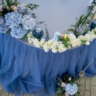 Beyaz çiçekler, mumlar ile dekore edilmiş düğün masası. Minderler ile yumuşak kanepe, büyük pencere. Mavi ve beyaz.