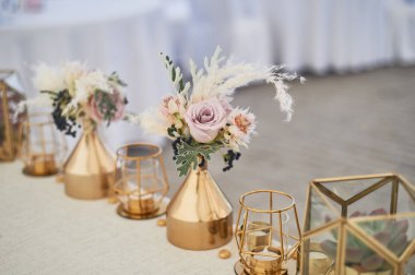 Boho tarzında düğün dekorasyonu. Açık renkler, çadırda. Gül ve tahıl ile altın vazolar ile dekore düğün masası. Ve altın mumlar geometrik mumlar.