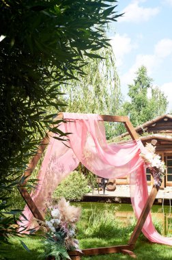 Göl kenarındaki ormana giriş yap. Pampalarla süslenmiş elmas şekilli ahşap kemer, pembe şifon. Düğün çiçekçisi..