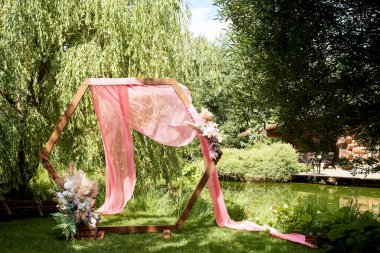 Göl kenarındaki ormana giriş yap. Pampalarla süslenmiş elmas şekilli ahşap kemer, pembe şifon. Düğün çiçekçisi..