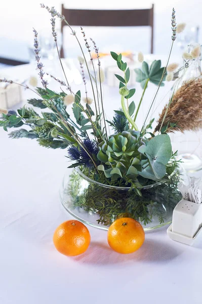 Zusammensetzung von Feldkräutern und Getreide auf dem Tisch im Restaurant in einem transparenten Gefäß. Weiße Tischdecke und zwei Mandarinen. Stilleben. — Stockfoto