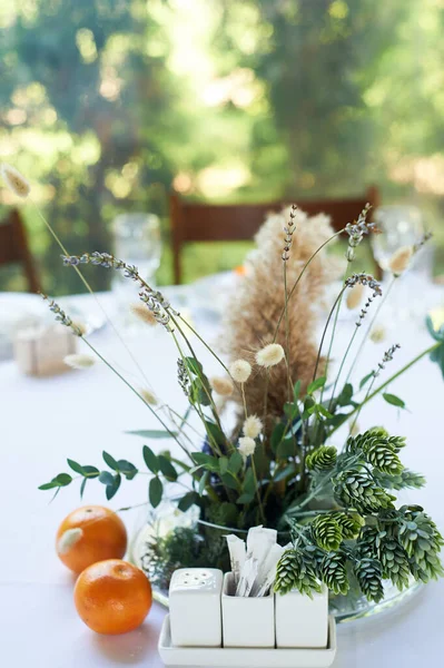 Composizione di erbe di campo e cereali in tavola nel ristorante in vaso trasparente.Tovaglia bianca e due mandarini. Moglie morta. — Foto Stock