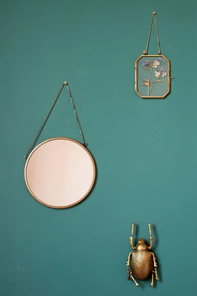 Parede verde, cor nobre.Pendurar um espelho, um besouro dourado e um herbário emoldurado. Decoração do interior . — Fotografia de Stock