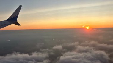 Şafak vakti bulutların üstünde bir uçak kanadı yüksekte uçar.