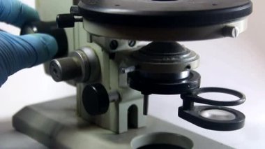 Doktorun eldivenli elinin yakın çekimi eski bir mikroskobu ayarlıyor.