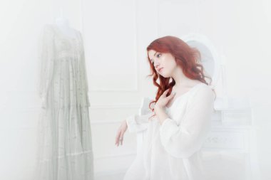 İhale portre nightdress içinde bir genç rüya gibi kızıl saçlı kadın. O elbise odasında oturuyor ve güzel vintage elbise giymek planlama