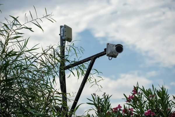 Görüntü, gölgeli bir gökyüzü ile bir direğe monte edilmiş bir güvenlik kamerası gösteriyor..