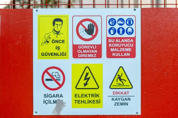 Kırmızı desenli bir yüzeye yerleştirilmiş, Türk dilinde altı güvenlik uyarısı ve tehlike sembolü içeren beyaz bir işaret.