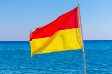 Sahilde kırmızı ve sarı bir cankurtaran bayrağı var. Arka planda okyanus ve mavi gökyüzü var..