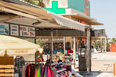 Tente altında turist eşyaları, giysileri ve aksesuarları sergilenen çeşitli dükkan ve tezgahların sokak manzarası ve arka planda bir bina.