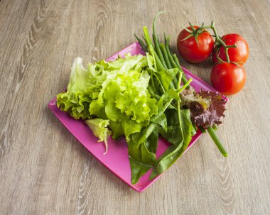 Yeşillikli salata, çeri domates, ahşap arka plan lı pembe kare tabaktabakta soğan, yakından görünümü