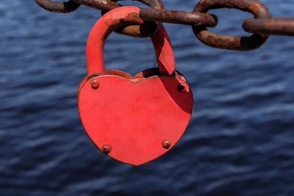 Love heart padlock on the rusty chain on the blue sea water background.