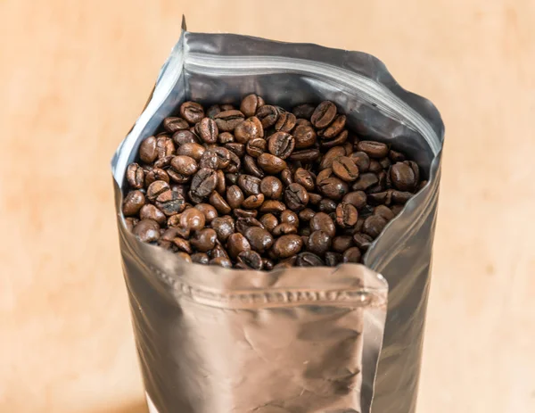 Coffee beans in a plastic foil package on wooden background.