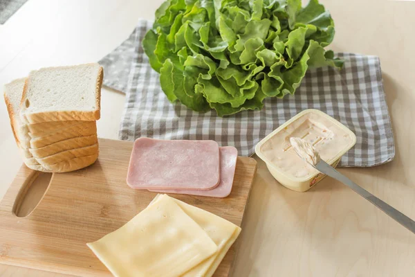 Kompozycja do produkcji kanapek z serem i szynką na drewnianym stole w jasnej kuchni. — Zdjęcie stockowe