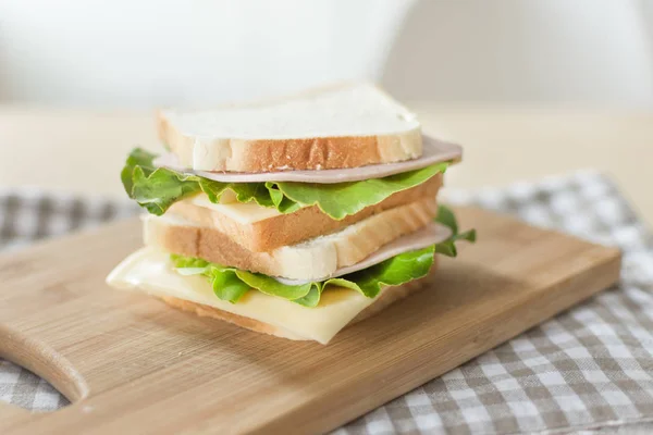 Sandwich mit Käse und Schinken auf Schneidebrett auf dem Tisch in der hellen Küche. — Stockfoto