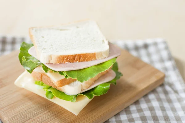 Sandwich with cheese and ham on cutting board on the table in the bright kitchen. — Stock Photo, Image