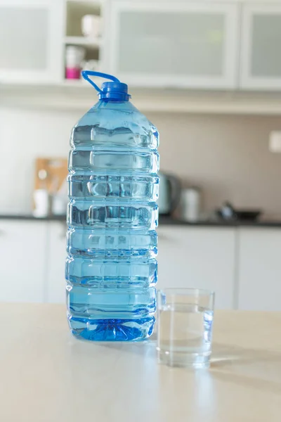 Большая пластиковая бутылка с водой на столе на ярком кухонном фоне . — стоковое фото