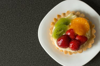 Siyah bir arka plan üzerinde krema, ahududu, kivi ve portakal ile Kek.