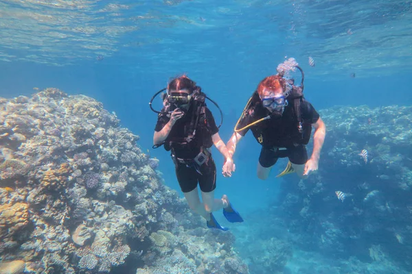 Человек в маске для подводного плавания и костюме ныряет под воду с тропическими рыбами в бассейне кораллового рифа . — стоковое фото