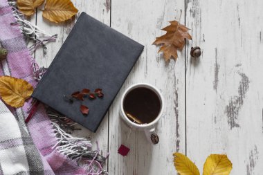 Kitap ile çay Fincan, ahşap masa üstü görünümünde sonbahar yaprakları.