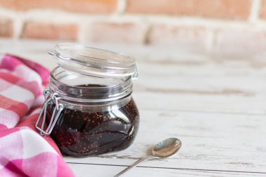 Ahşap masa üzerinde cam bir kavanozda ahududu reçeli.