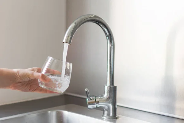 Kädet keittiössä ottamassa lasillista vettä keittiön pesualtaalla kotona . — kuvapankkivalokuva