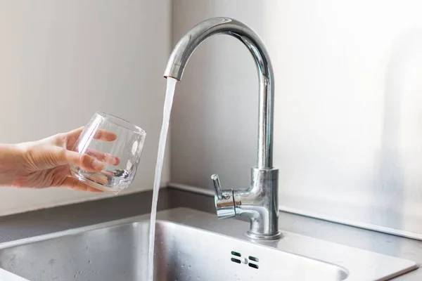 Kädet keittiössä ottamassa lasillista vettä keittiön pesualtaalla kotona . — kuvapankkivalokuva