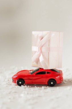 Kar ile beyaz arka plan üzerinde bir Noel hediyesi taşıyan Oyuncak araba.