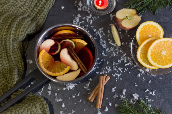 Petite casserole avec vin chaud et bâtonnets de cannelle, tranche d'oranges et pomme sur table sombre vue sur le dessus . — Photo