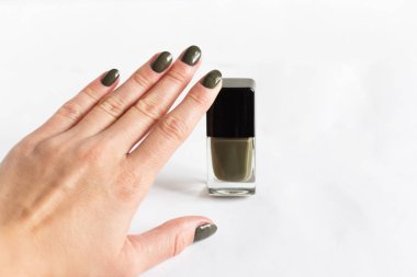 Beautiful female hands with modern khaki manicure and nail polish bottle with brush.