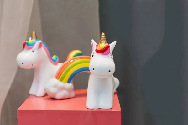 Ceramic souvenir unicorn toy money box with colorful rainbow on pink table.