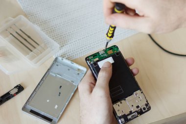 İnsan eli tornavida üstünde okul sırası ile cep telefonu tamiri.