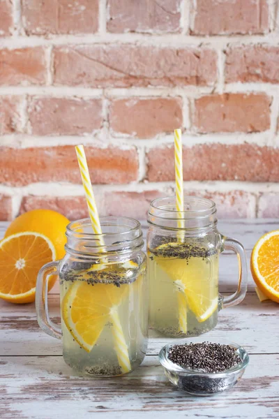 Semillas de chía agua de desintoxicación. Bebida saludable con rebanada de fruta naranja en frascos de vidrio manson y beber paja en la mesa de madera con frutas de naranja . — Foto de Stock