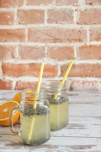 Semillas de chía agua de desintoxicación. Bebida saludable con rebanada de fruta naranja en frascos de vidrio manson y beber paja en la mesa de madera con frutas de naranja . — Foto de Stock