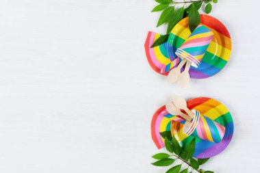 Gökkuşağı renkli tek kullanımlık tabaklar beyaz ahşap arka plan manzaralı. Doğum günü partisi çevre dostu yemekler, piknik malzemeleri. Boşluğu kopyala.