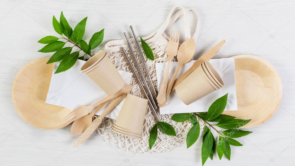 Eco friendly disposable dishes made of bamboo wood and paper on white wooden background. Sustainable lifestyle concept.
