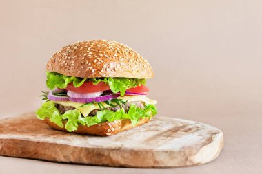 Tahta kesme tahtasında taze salata, peynir ve domatesli sığır burger. Fast food, sağlıksız yemek..