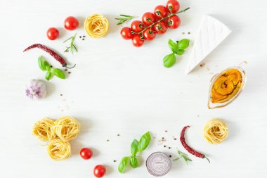 Yemek pişirmek için İtalyan makarna malzemesi çerçevesi. Çiğ makarna, peynir, sebze, baharat ve otlar beyaz ahşap arka planda üstten görünüyor. İtalyan sağlıklı vejetaryen yemekleri.