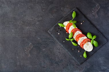 Mozarellalı Caprese salatası, domates, taze zeytin yağı ve fesleğen. Siyah arka plan manzaralı. Lezzetli İtalyan vejetaryen salatası.