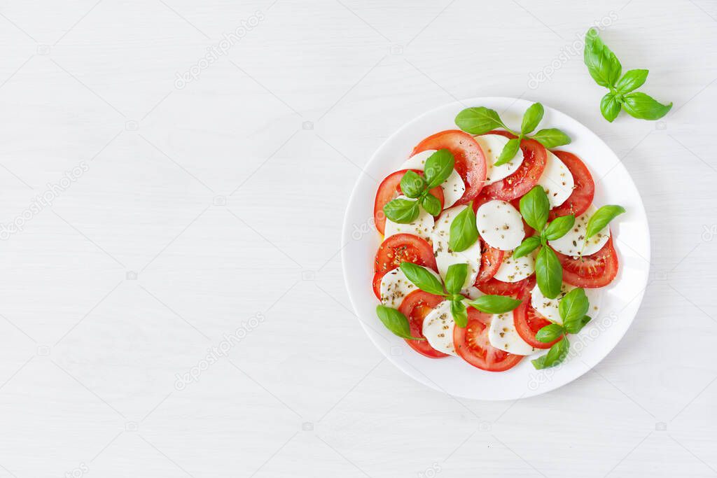 Caprese salad with mozzarela, tomatoes, fresh olive oil and basil on white background top view. Delicious italian vegan salad.