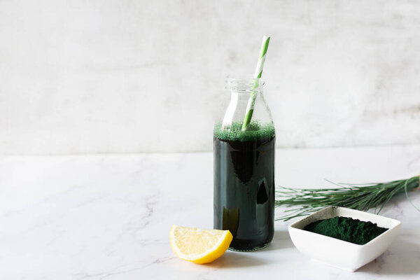 Spirulina drink with lemon and spirulina algae powder on white marble table. Superfood, detox drink.