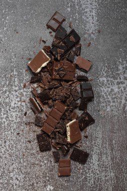 Kesilmiş, öğütülmüş, koyu ve sütlü çikolata dilimleri ve gri arka planda talaş yığınları..