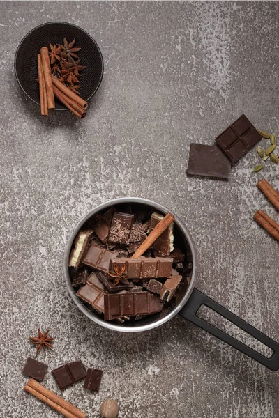 Kesilmiş, öğütülmüş, koyu ve sütlü çikolata dilimleri ve gri arka planda baharatlarla dolu bir tencerede talaş..