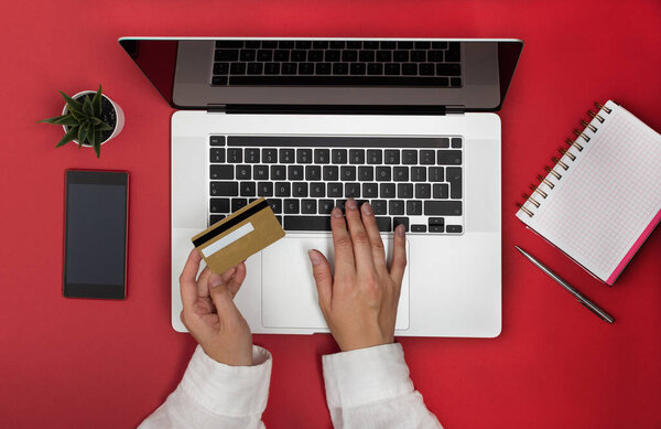 Женские руки с помощью кредитной карты для покупок в Интернете или банковский вид сверху на красном фоне.