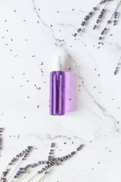 Bottle of skincare tonic water with dried lavender herbs top view on white marble background top view. Vertical orientation.