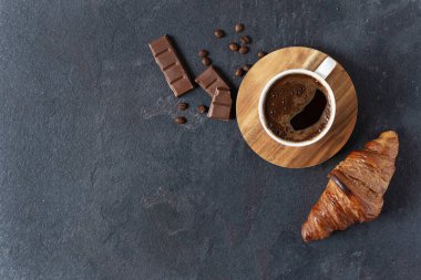 Bir fincan kahve, çikolatalı kruvasan ve siyah arka plan manzaralı fotokopi alanı..