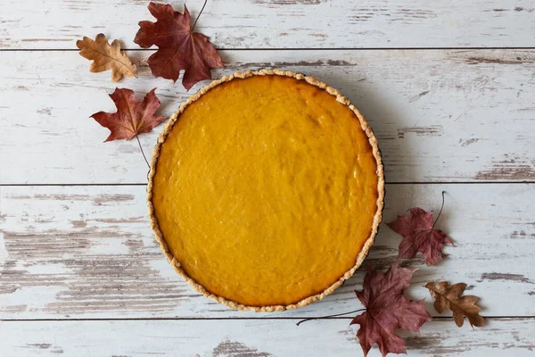 Fresh homemade pumpkin pie in a baking dish on white wooden table top view. Traditional american pumpkin pie.