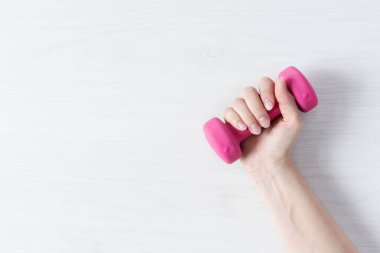 Beyaz ahşap arka plan manzarası üzerinde pembe dambılı tutan bir kadın. Fitness ekipmanları. 