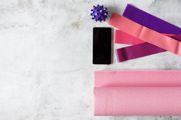Spor lastikleri, yoga minderi, masaj topu ve gri beton zeminde akıllı telefon. Spor aletleri düz konumda. Çevrimiçi çalışma kavramı.